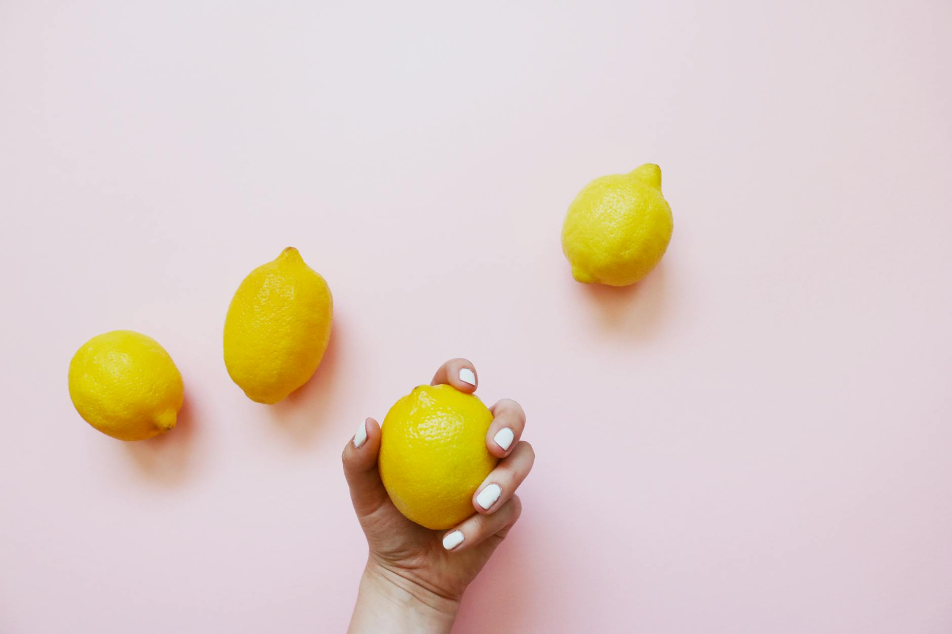 A hand holding a fresh lemon on a soft pink background, symbolizing renewal and fresh starts.