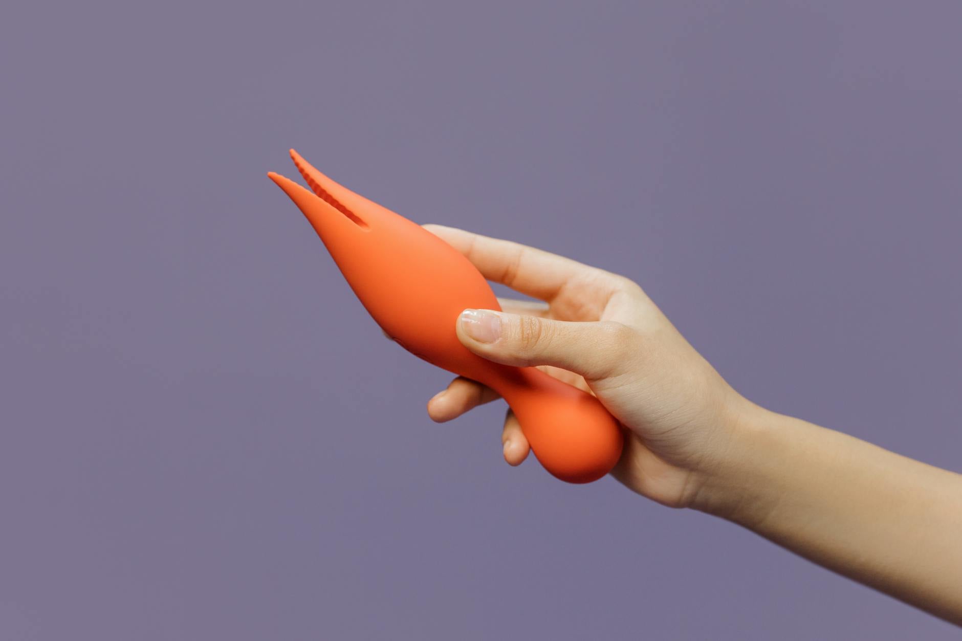 Close-up of a hand holding a lemon-colored vibrator against a minimalistic backdrop, showcasing modern sensual design.
