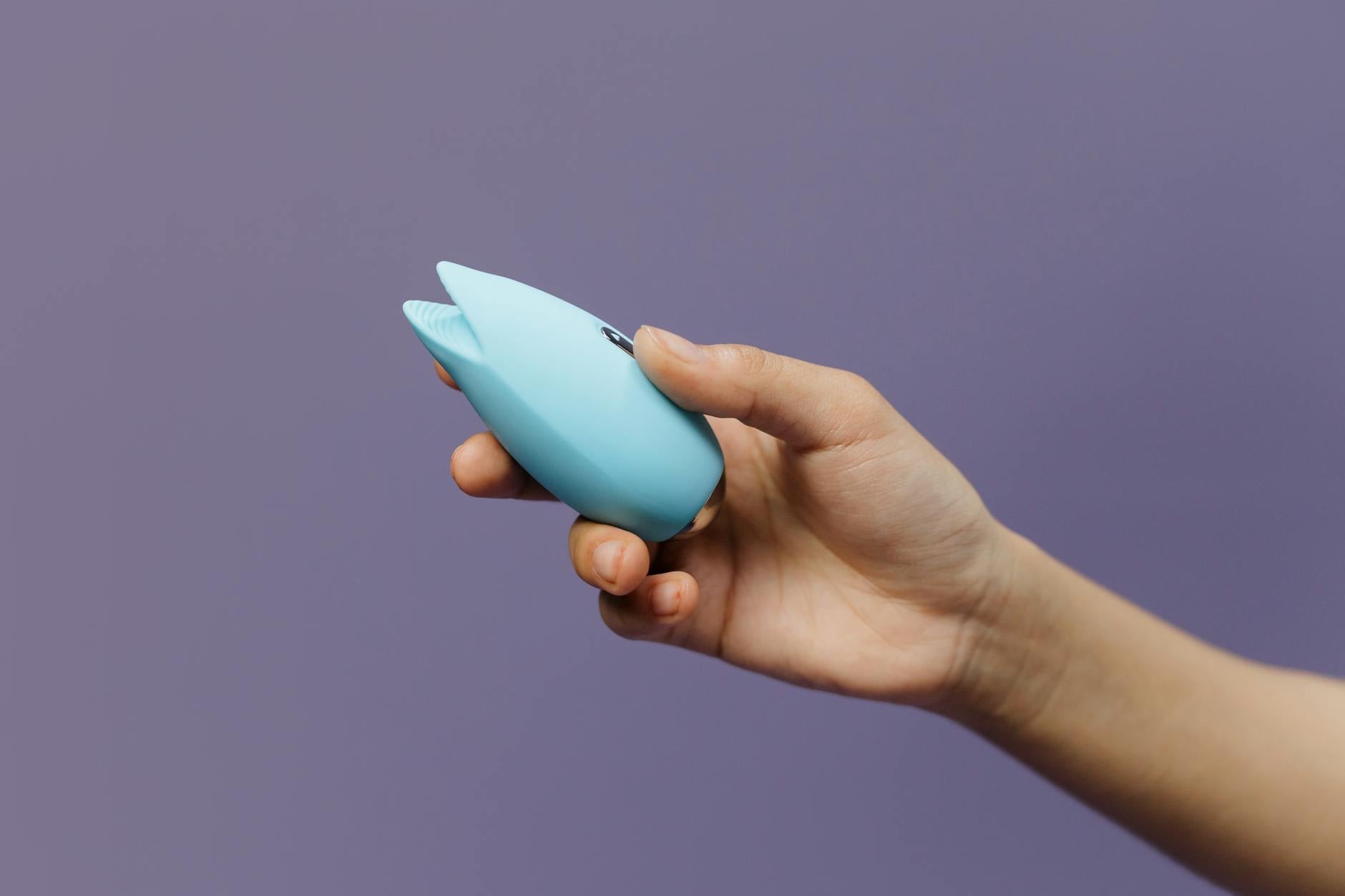 A blue silicone vibrator held in hand against a solid purple background, promoting self-love and pleasure.