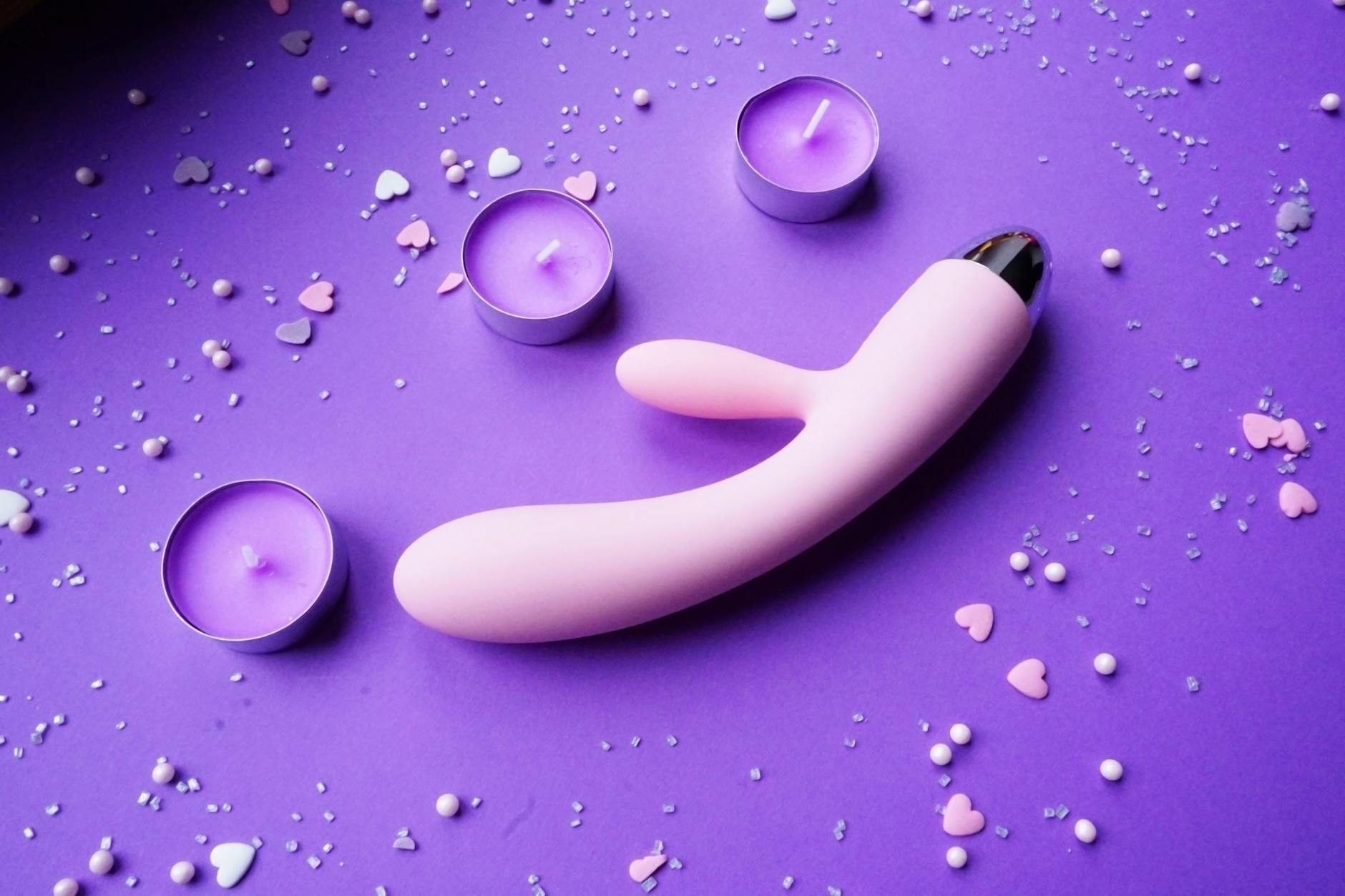 Pink lemon vibrator on purple background with heart confetti and candles for a romantic atmosphere